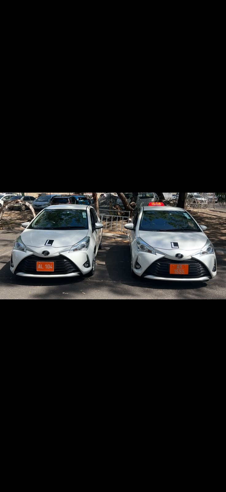 Wide view of two white IQ Driving School learner vehicles